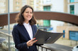 © Mangostar - Cheerful businesswoman holding folder. Smiling middle aged businesswoman in formal wear holding papers and looking aside on street. Professional occupation concept