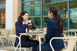 © Mangostar - Businesswomen drinking coffee in outdoor cafe. Female colleagues in formal wear sitting at table and drinking coffee together. Coffee time concept