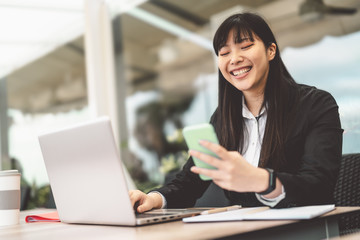 Business Asian woman using mobile smartphone and computer outdoor - Happy Chinese girl working on laptop in office - Professional job and people with technology concept