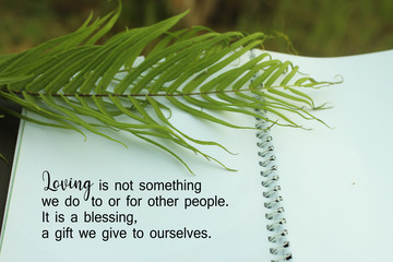 Inspirational quote - Loving is not something we do to or for other people. It is blessing, a gift we give to ourselves. With green palm leaf and text on white spiral note book. 