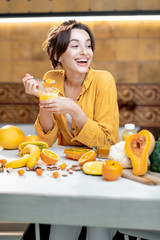 Wall Mural - Young and cheerful woman eating chia pudding, having a snack or breakfast in the kitchen with lots of fresh fruits and vegetables. Concept of vegetarianism, healthy eating and wellness