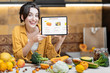 © rh2010 - Woman holding digital tablet with launched online shopping market while standing on the kitchen with lots of fresh food on the table