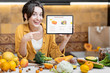 © rh2010 - Woman holding digital tablet with launched online shopping market while standing on the kitchen with lots of fresh food on the table
