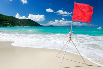 Wall Mural - bright sunny view of red flag standing in the waves of a tropical island beach