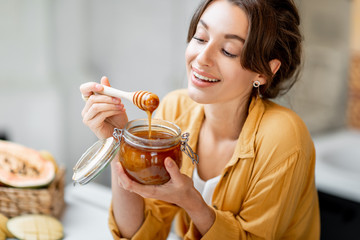 Portrait of a young and cheerful woman with a jar full of sweet honey on the kitchen at home