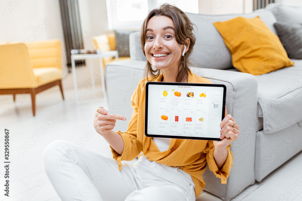 Young and cheerful woman showing a digital tablet screen with launched online store, shopping online at home. Concept of buying online using mobile devices - obrazy, fototapety, plakaty 