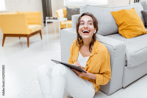 Fotomural Young and cheerful woman working on digital tablet while sitting relaxed on the floor at home