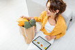 © rh2010 - Young woman shopping online using a digital tablet, sitting with bag full of products at home. Concept of buying online using mobile devices