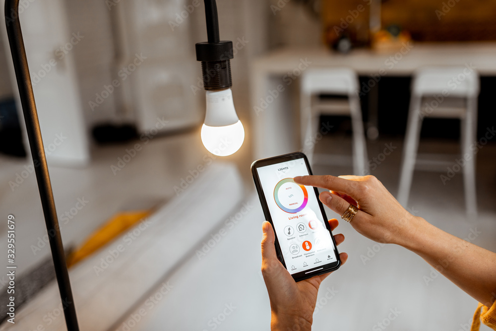 Controlling light bulb temperature and intensity with a smartphone application. Concept of a smart home and managing light with mobile devices - obrazy, fototapety, plakaty 