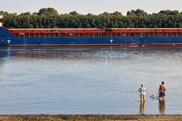 Wall Mural - Fishermen on the river bank and cargo ship