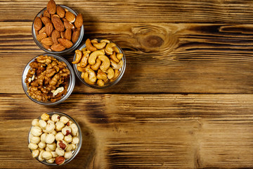 Sticker - Assortment of nuts on wooden table. Almond, hazelnut, walnut and cashew in glass bowls. Top view, copy space. Healthy eating concept