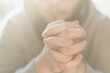 Bearded adult man praying to God sitting at home in the sunbeam. A Muslim or Christian raises his hands to God. Crossed hands in prayer gesture close up