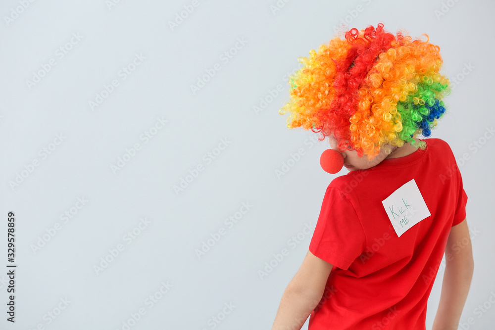 Sticky note with text KICK ME on back of little boy against light background. April Fools' Day celebration