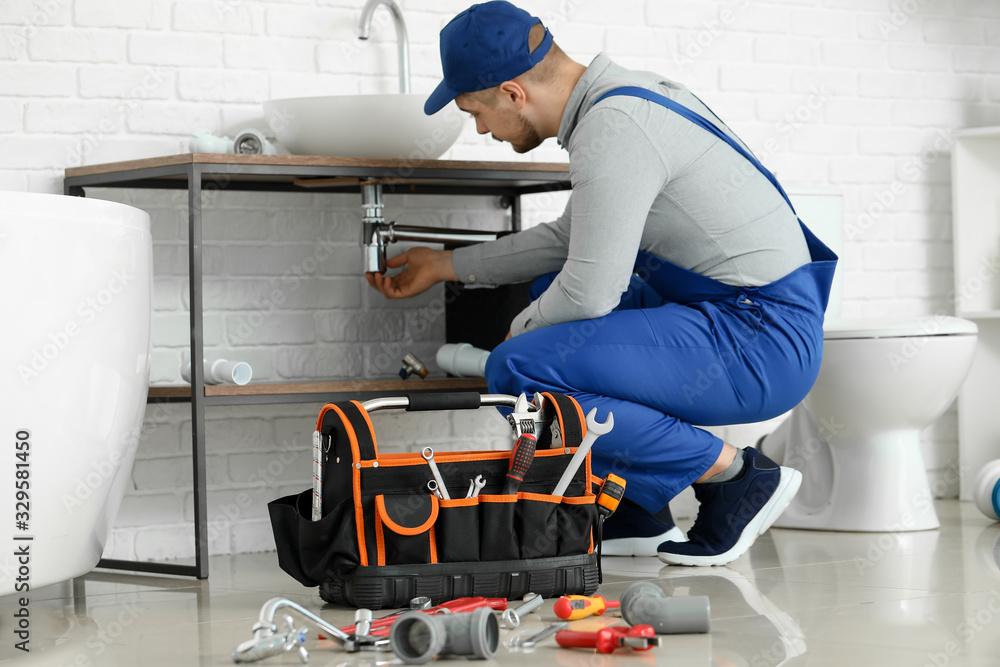 Handsome plumber repairing sink in bathroom