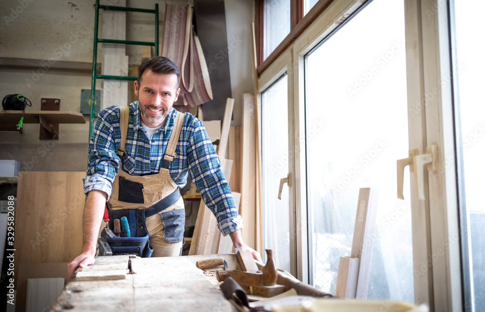Portrait of mature carpenter posing in his carpentry workshop with tools in background - obrazy, fototapety, plakaty 