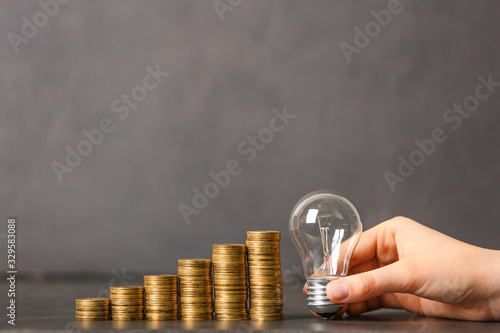 Female hand with light bulb and coins on grey background. Concept of savings money