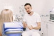 © etonastenka - The dentist tells how to care for braces using the example of an artificial jaw. A woman, a dentist client, sits in a dental chair and listens to a doctors story about oral hygiene