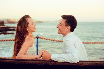 The concept of rest, vacation, travel, honeymoon. A girl and a guy are sitting on a bench, laughing against the backdrop of the ocean and mountains. Spain, Canaries.