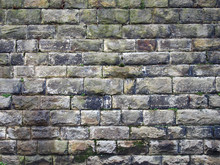 An Old Grey Damp Stone Wall Made Of Large Regular Blocks Covered In Patches Of Moss