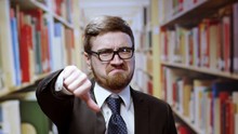 Dissatisfied Young Caucasian Businessman In Suit Showing Negative Sign Thumbs Down Of Disregard Looking Upset Posing Near Bookshelves In The Library.