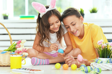 Little brother and sister painting traditional Easter eggs in different colors at home, with pleasure preparing to religious spring holiday