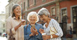 © VAKSMANV - Three beautiful and cheerful Caucasian women with coffee to-go in hands laughing while scrolling photos on smartphone outdoor. Happy joyful grandmothers smiling while watching pictures on smartphone.