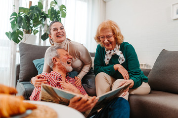 Happy family laughs while watching at old photos from family photo album while sitting in living room.