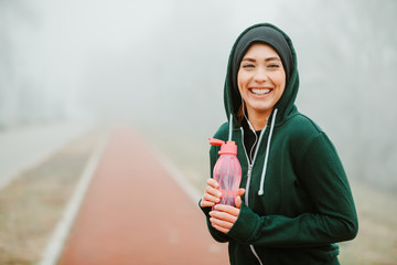 Wall Mural - Close shot of smiling young girl who is holding pink water bottle posing on running track.