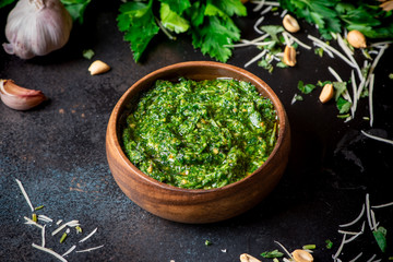 Homemade pesto sauce in a wooden bowl and ingredients for cooking on a black background close-up. Italian food.