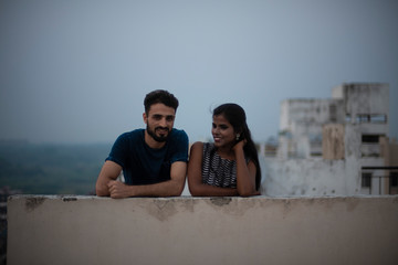 A dark skinned Indian/African girl in  western dress and a Kashmiri/European/Arabian man in casual wear spending time on a rooftop in the afternoon in urban background. Lifestyle of a couple.