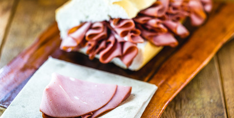 Wall Mural - mortadella, pork slices, on italian bread, on rustic wooden background. A mortadella sandwich is any sandwich using mortadella, a large Italian sausage, and is a very popular sandwich in Brazil.