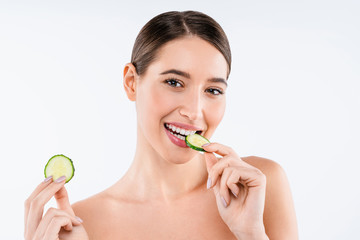 Wall Mural - Beauty portrait of smiling young topless woman eating slice of cucumber standing isolated over white background