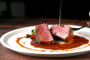 Wall Mural - Beef tenderloin steak in demiglas sauce is cut with a knife on a white platter