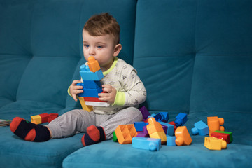 The kid is playing constructor sitting on a blue sofa. Educational games for children. The boy collects blocks of the constructor.