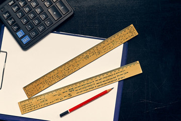 Education concept. Calculator and pencil over a sheet of paper and wooden rulers with maths formulas.