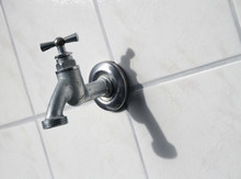 Closeup Of Of Silver Hose Bibb / Stopcock On Wall With White Tiles, Symbol For Water Wasting And Dripping