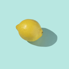 Whole yellow juicy lemon with shadow on a light blue (turquoise) background.