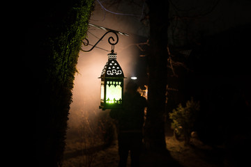 Beautiful colorful illuminated lamp in the garden in misty night. Retro style lantern at night outdoor.