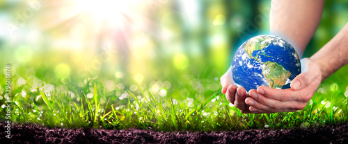 Fotografía Hands Holding Planet Earth In Lush Green Environment With Soil And Sunlight - Ea