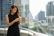© Ranta Images - Young beautiful Asian businesswoman using phone against view of the city