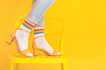 Legs of young woman in socks and sandals standing on chair against color background