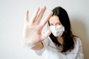 On a light background, a brunette woman in a white medical coat with gray accents and a protective mask on her face closeup in the center of the frame. Left hand in focus