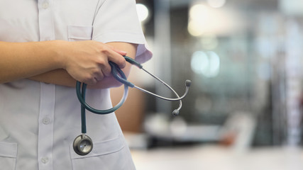 Cropped image of doctor holding a stethoscope while standing in hospital with blurred background