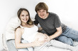 © Mangostar - Happy expectant couple posing at home. Young man touching pregnant wife belly, looking at camera, smiling. Expecting parents concept