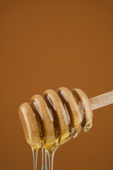 Poster - Honey dripping from honey dipper. Thick honey dipping from the wooden honey spoon. yellow background. closeup