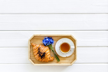 Wall Mural - Breakfast with summer flowers. Tea, croissant and cornflowers on white wooden background top-down copy space