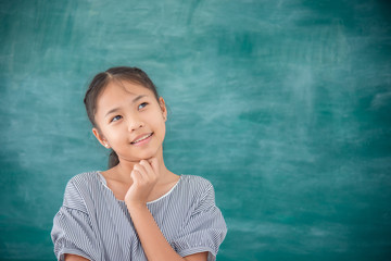 Young asian female student thinking and smiles in front of green chalkboard background.