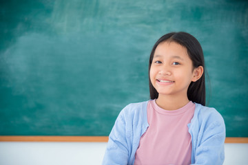 Young asian female student standing and smiles in front of green chalkboard background.