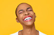 Happy ecstatic African American woman smiling with eye closed isolated on colorful yellow background