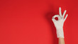 © nisara - A Okay hand sign with gloves in right hand on red background.